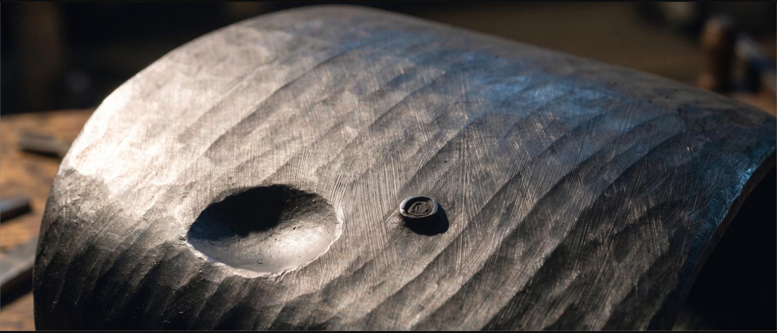 Close view of hammer marks and a small stamped maker's mark on dark forged steel